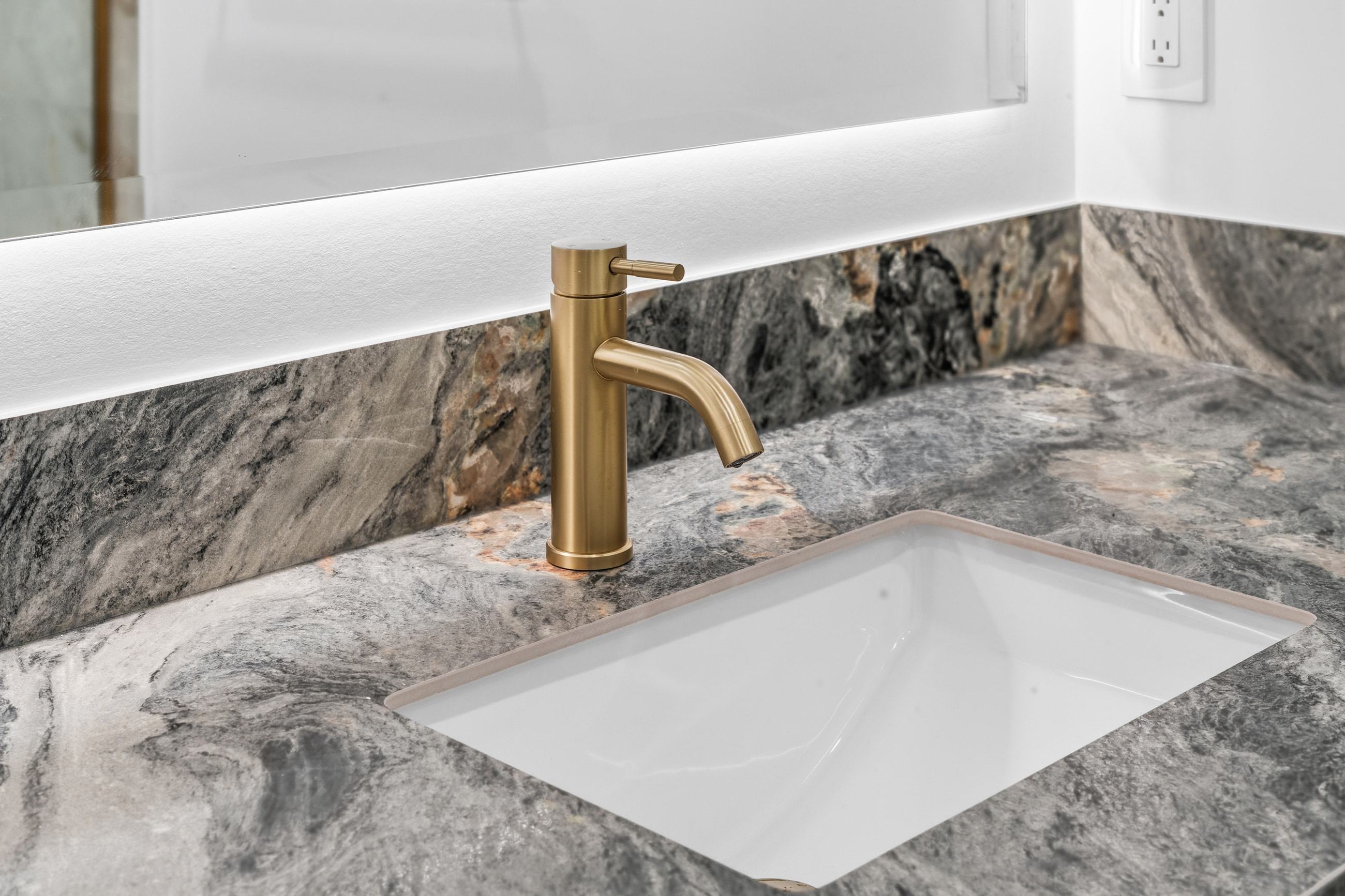 A brushed brass faucet where it meets the stone counter and the undermount basin.