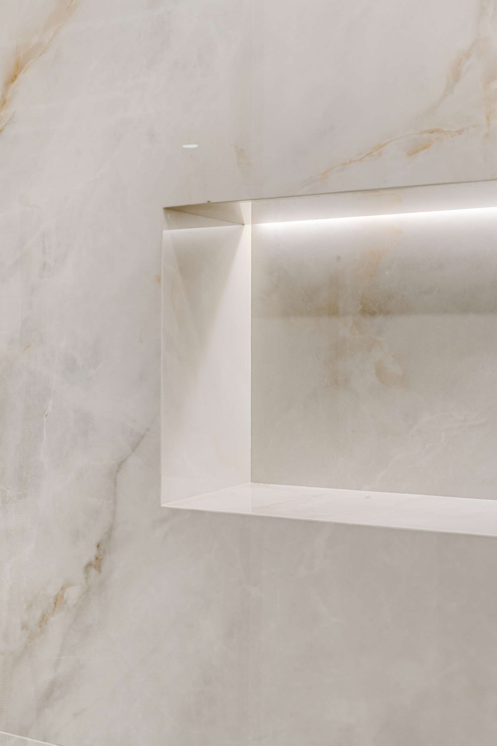 The illuminated niche cut into the porcelain, its edges mitred so the stone folds at the corner.