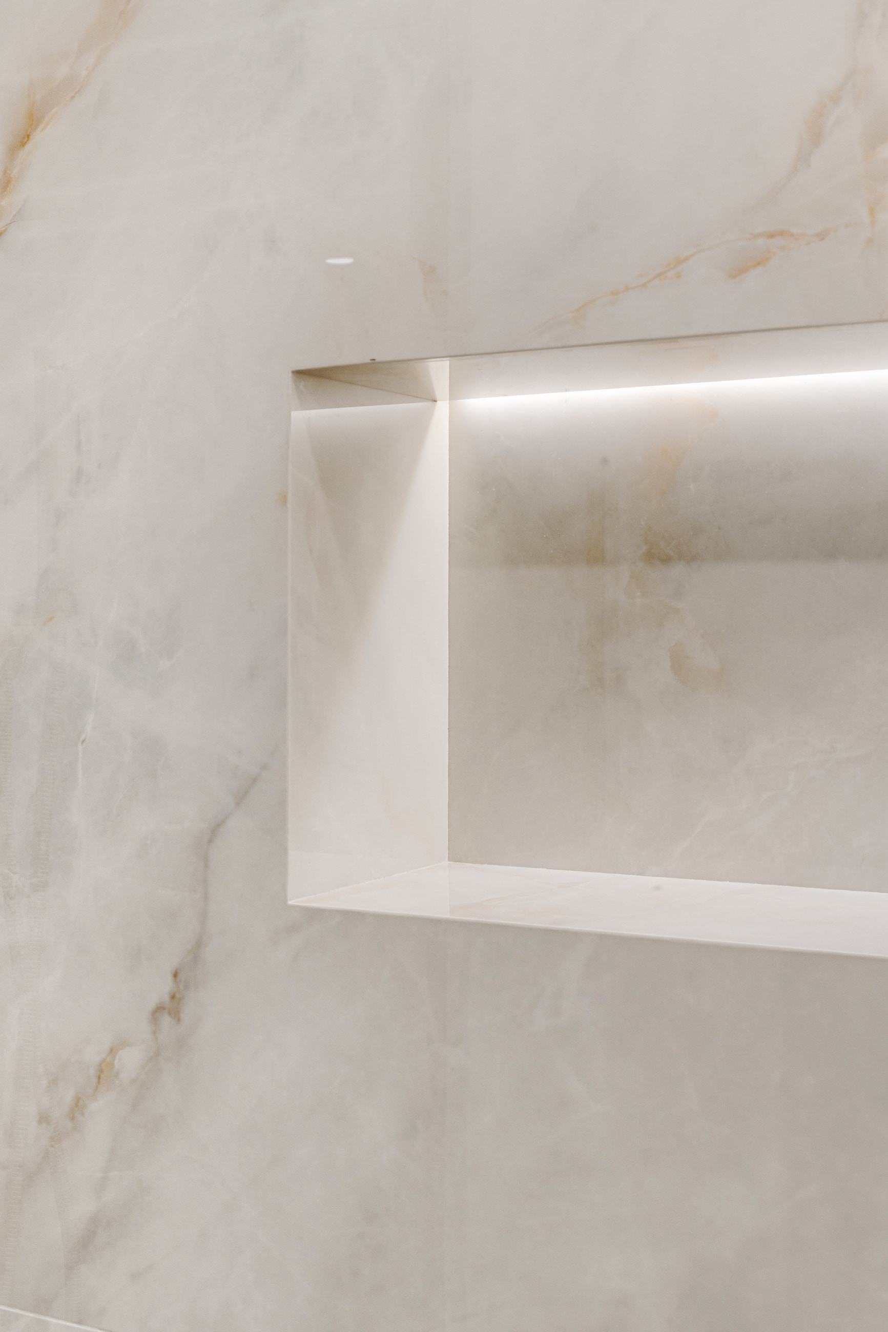 The illuminated niche cut into the porcelain, its edges mitred so the stone folds at the corner.