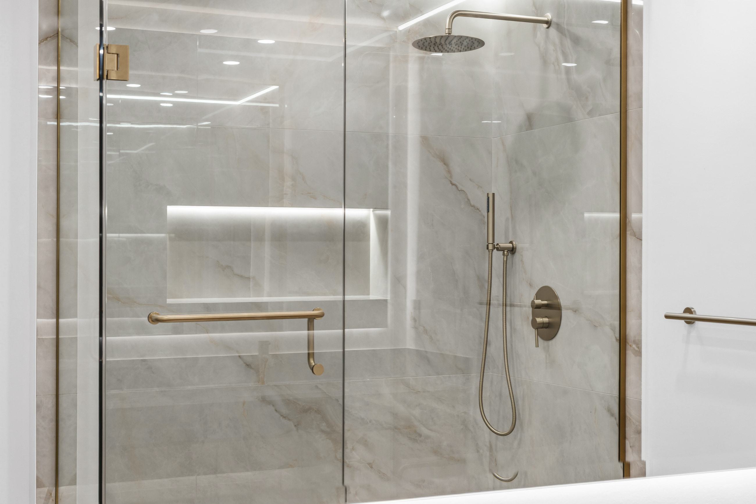The shower seen through brass-framed glass, with a grab bar and an illuminated niche in bookmatched porcelain.
