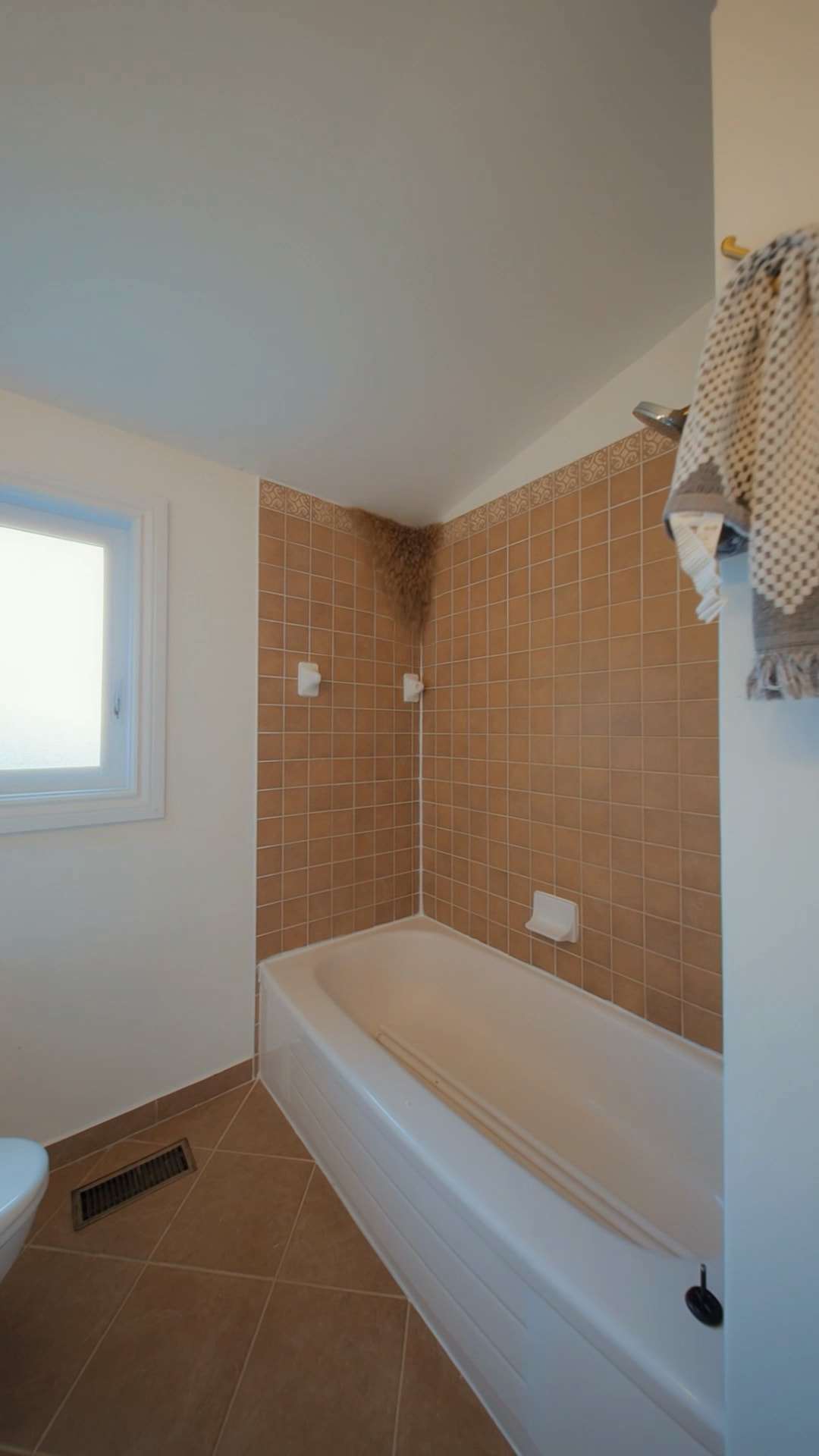 Before: a tub in a small-tiled alcove with a metal floor register beside it.