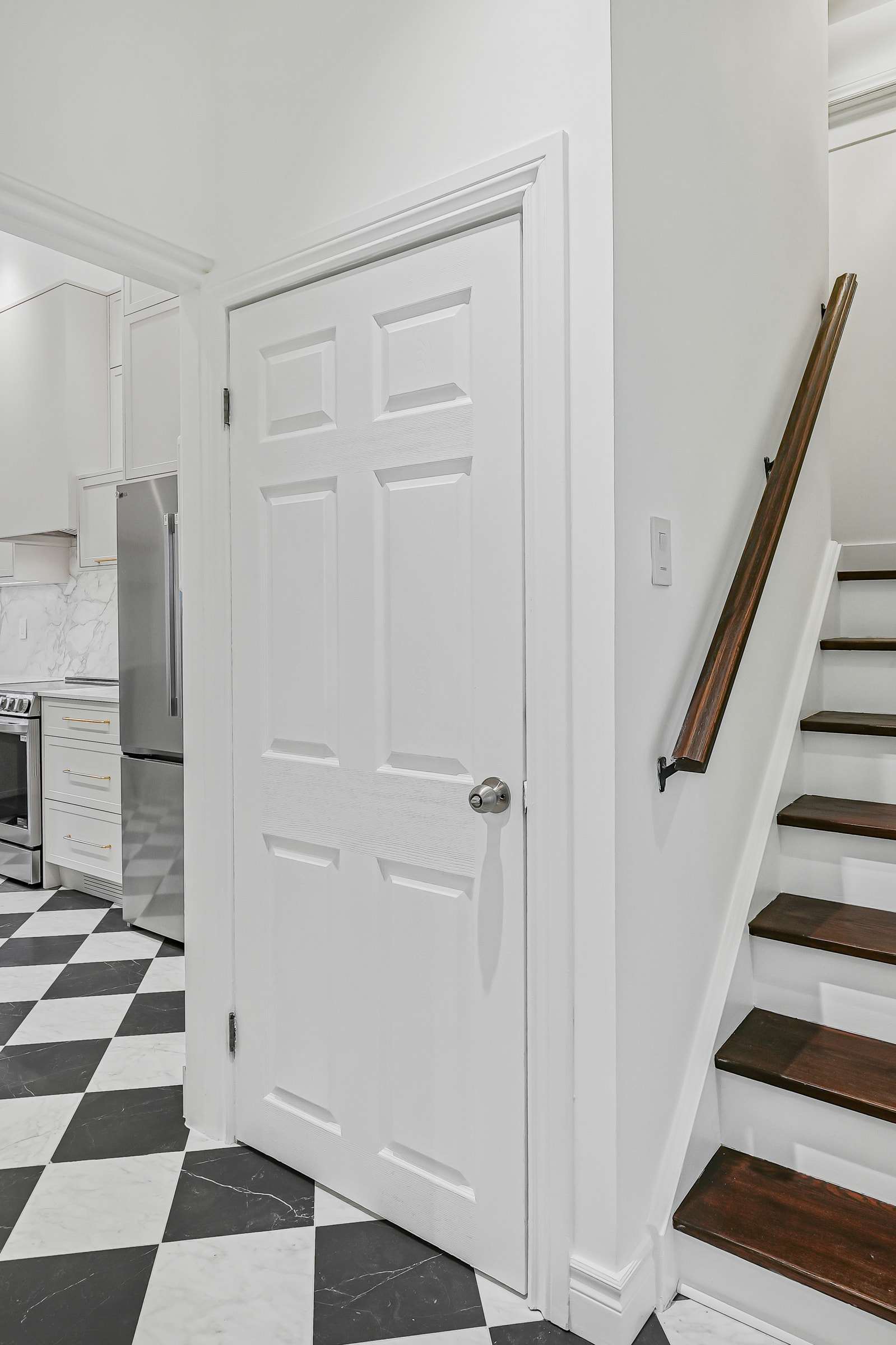 Stairs off the entry with dark treads and a wall-mounted rail, beside a panelled door.