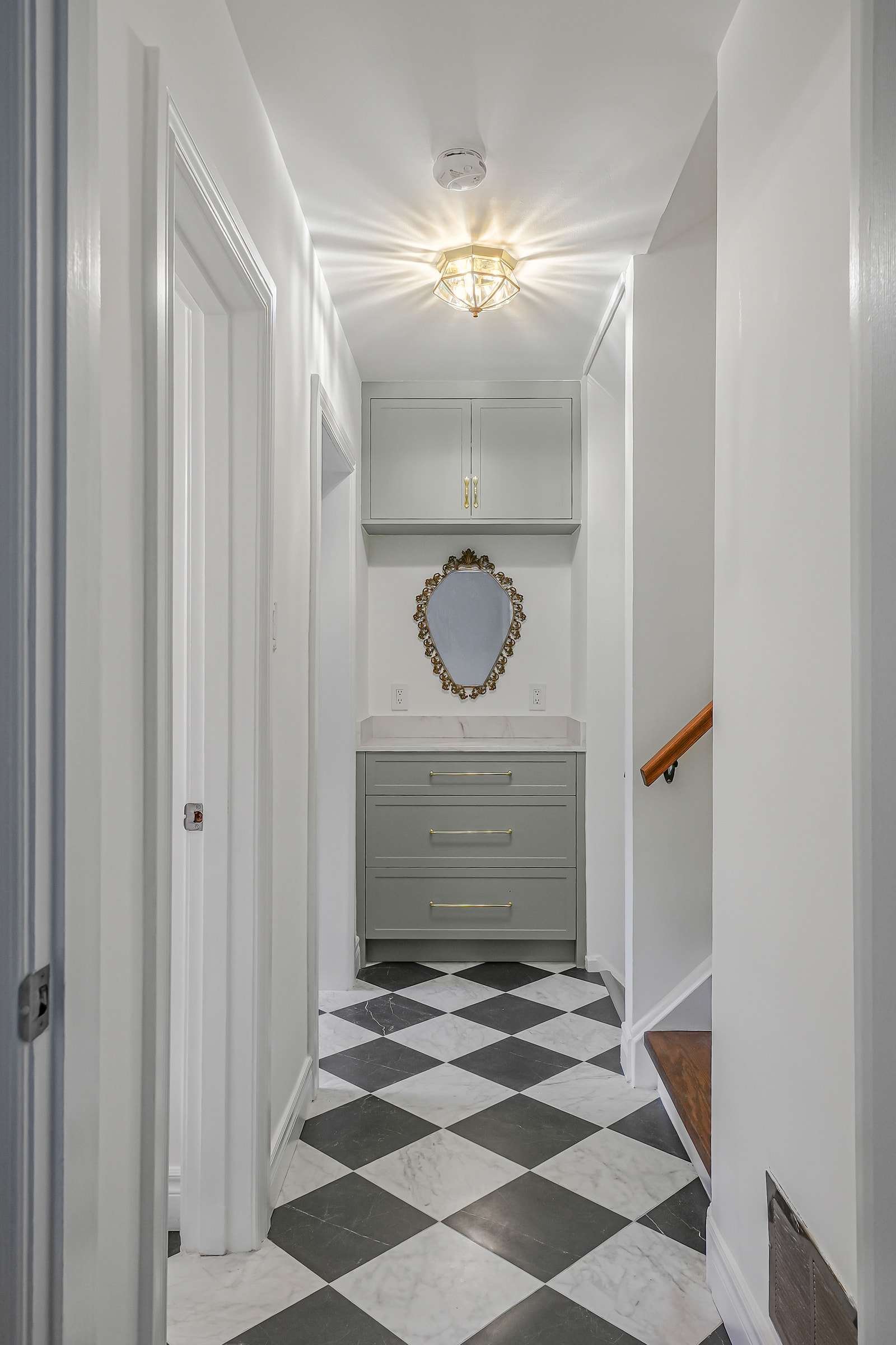 A hall ending at a sage built-in with drawers and a gilt mirror, under a glass ceiling light.