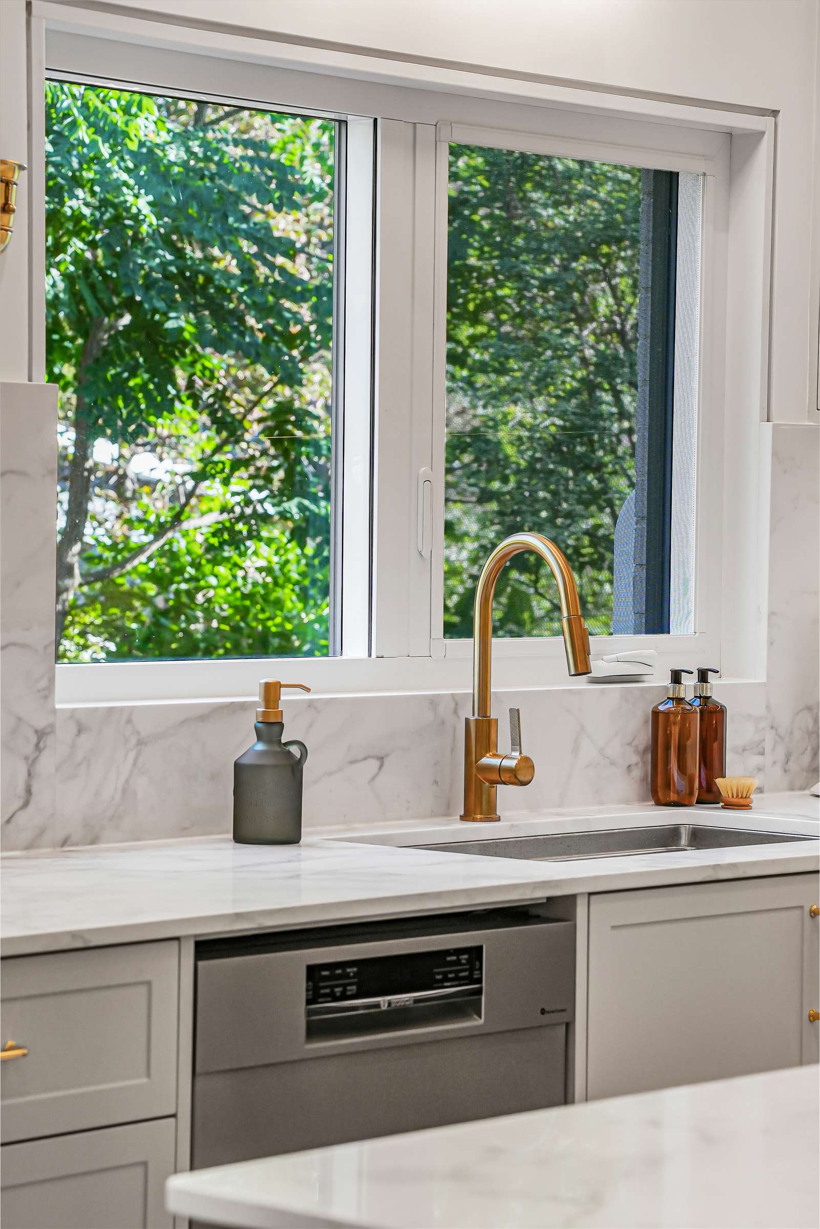 The faucet and sink under the window, trees outside.