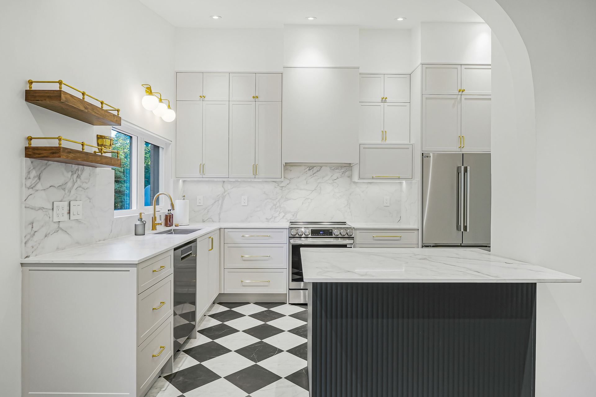 The Guildwood kitchen by TruBilt: tall white cabinetry, a fluted dark green island and a black-and-white floor, opened up through a wide arch.