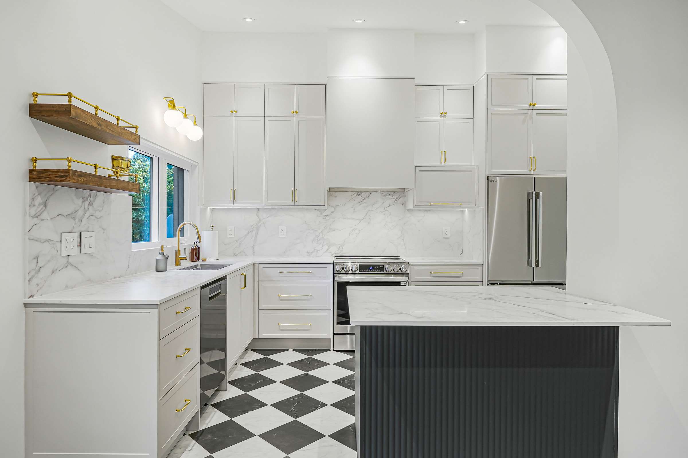 The finished Guildwood kitchen: tall white cabinetry, a fluted dark green island and a black-and-white floor, framed by the new arch.