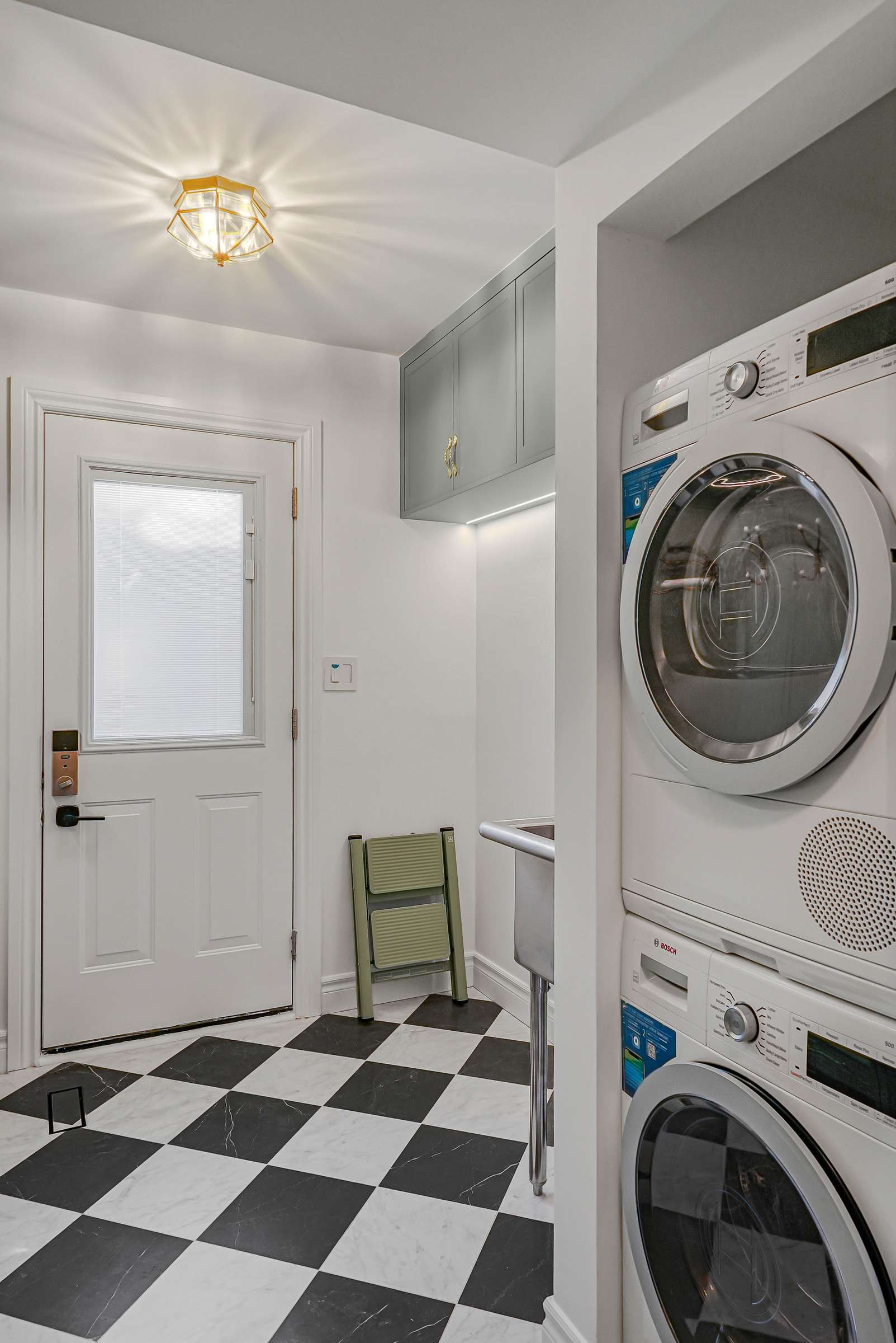 Stacked washer and dryer beside the side door, sage cabinets above with a light line beneath.