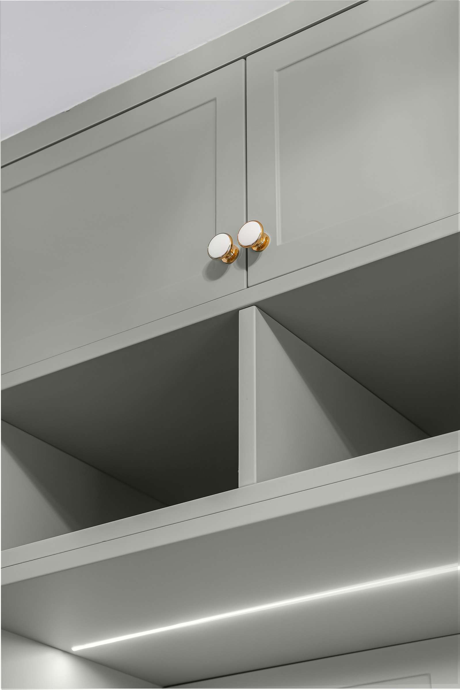 Open cubbies under sage cabinet doors, a light line along the shelf.