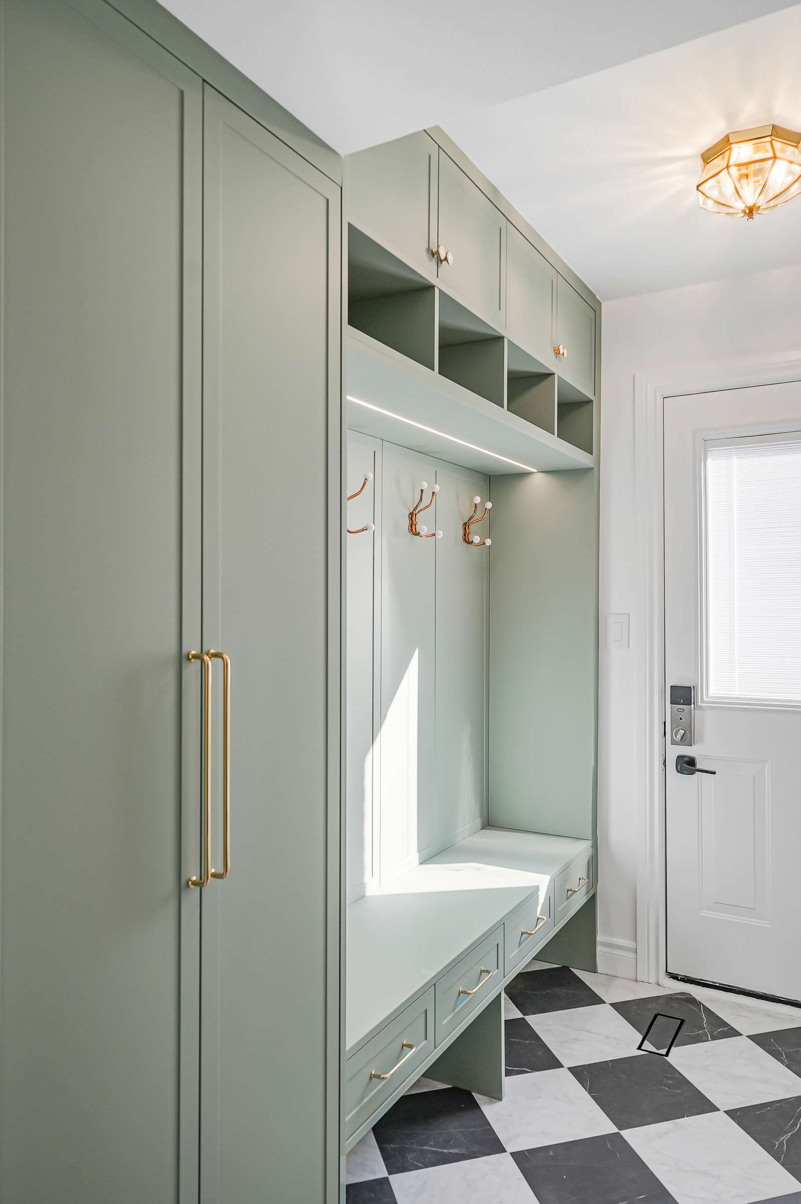The mudroom: tall sage lockers, a bench with hooks and lit cubbies, and the side door.