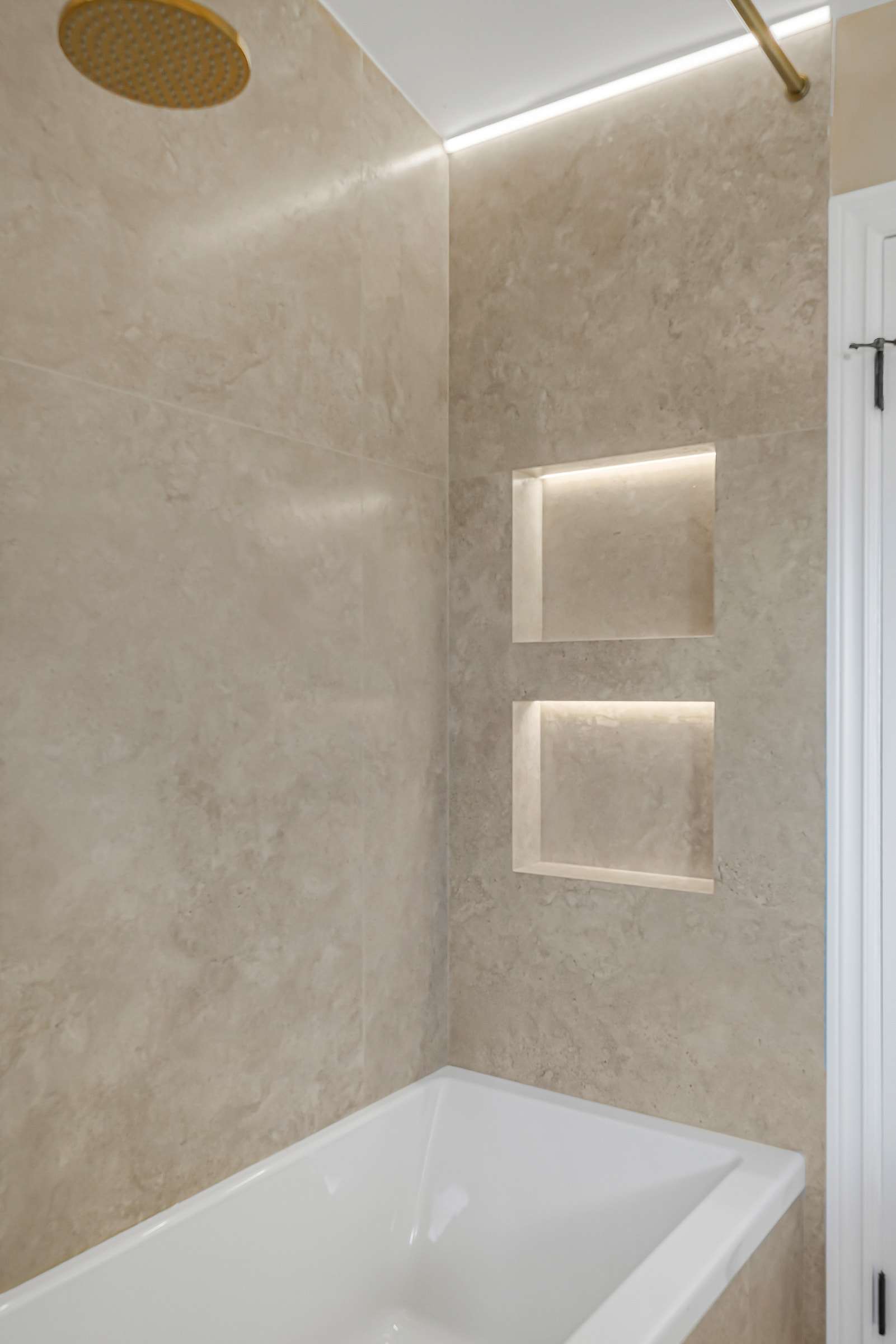 Two lit niches set into the wall above the tub, a light channel along the ceiling.