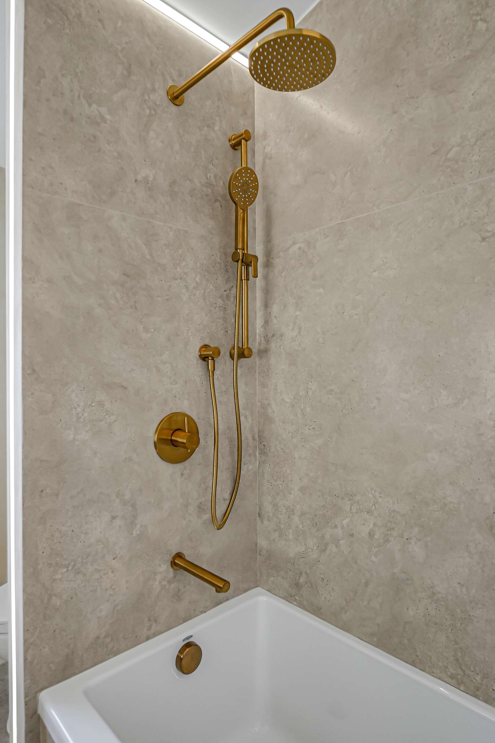 A rain head and hand shower on a slide bar above the tub, a light line along the ceiling.