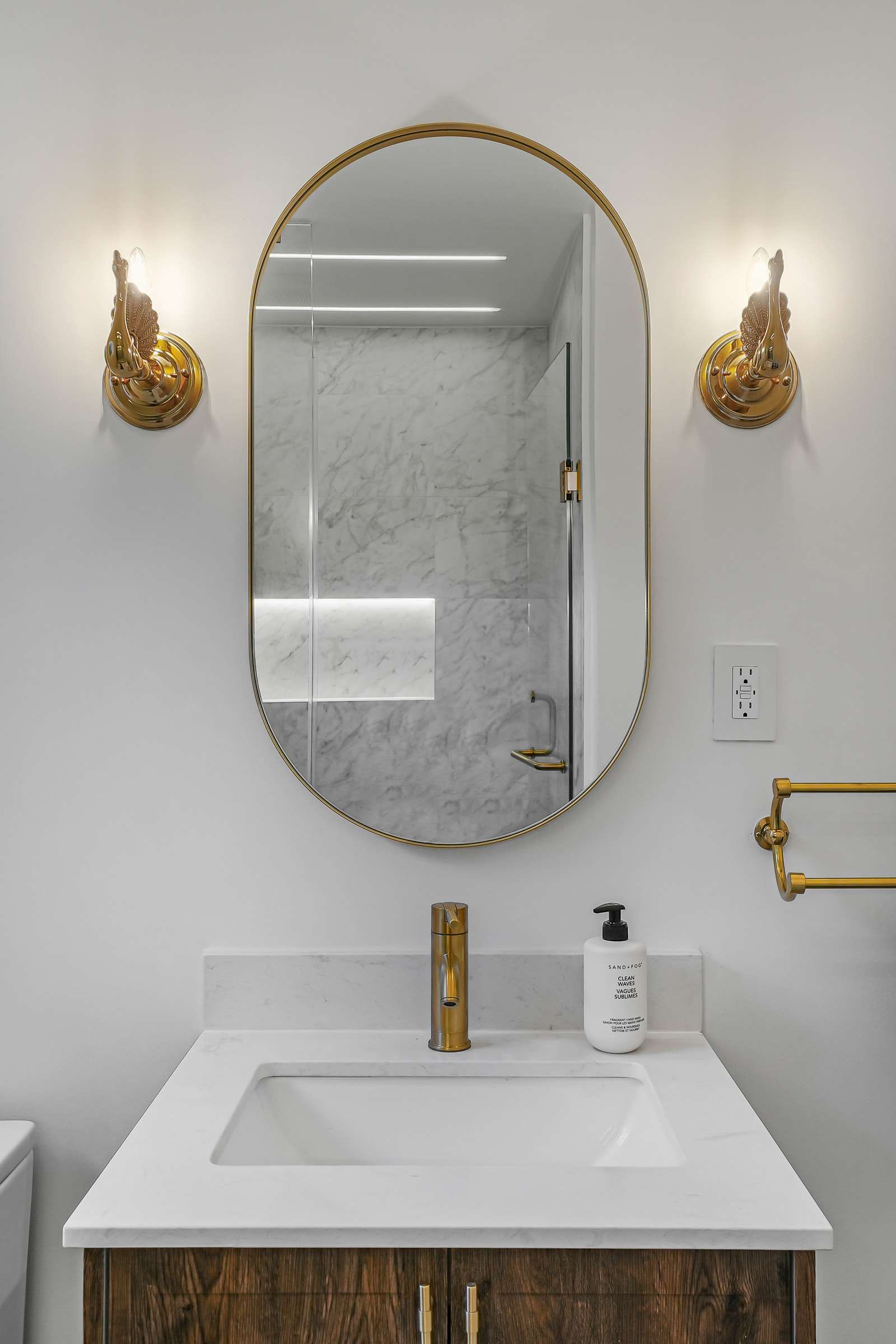 A small vanity under an oval mirror, a swan sconce on each side.
